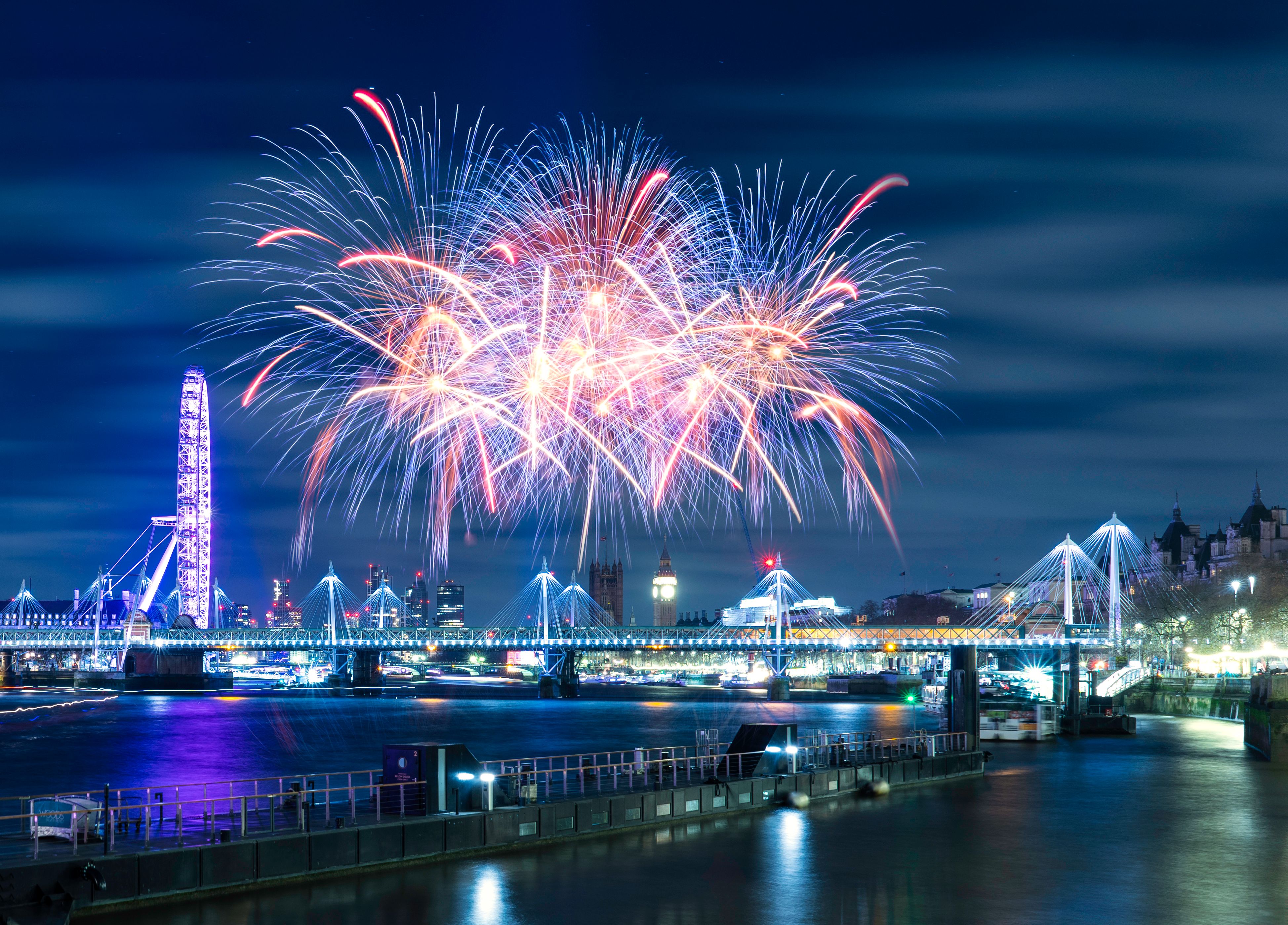 Fireworks illuminate London's skyline over the Thames at night.