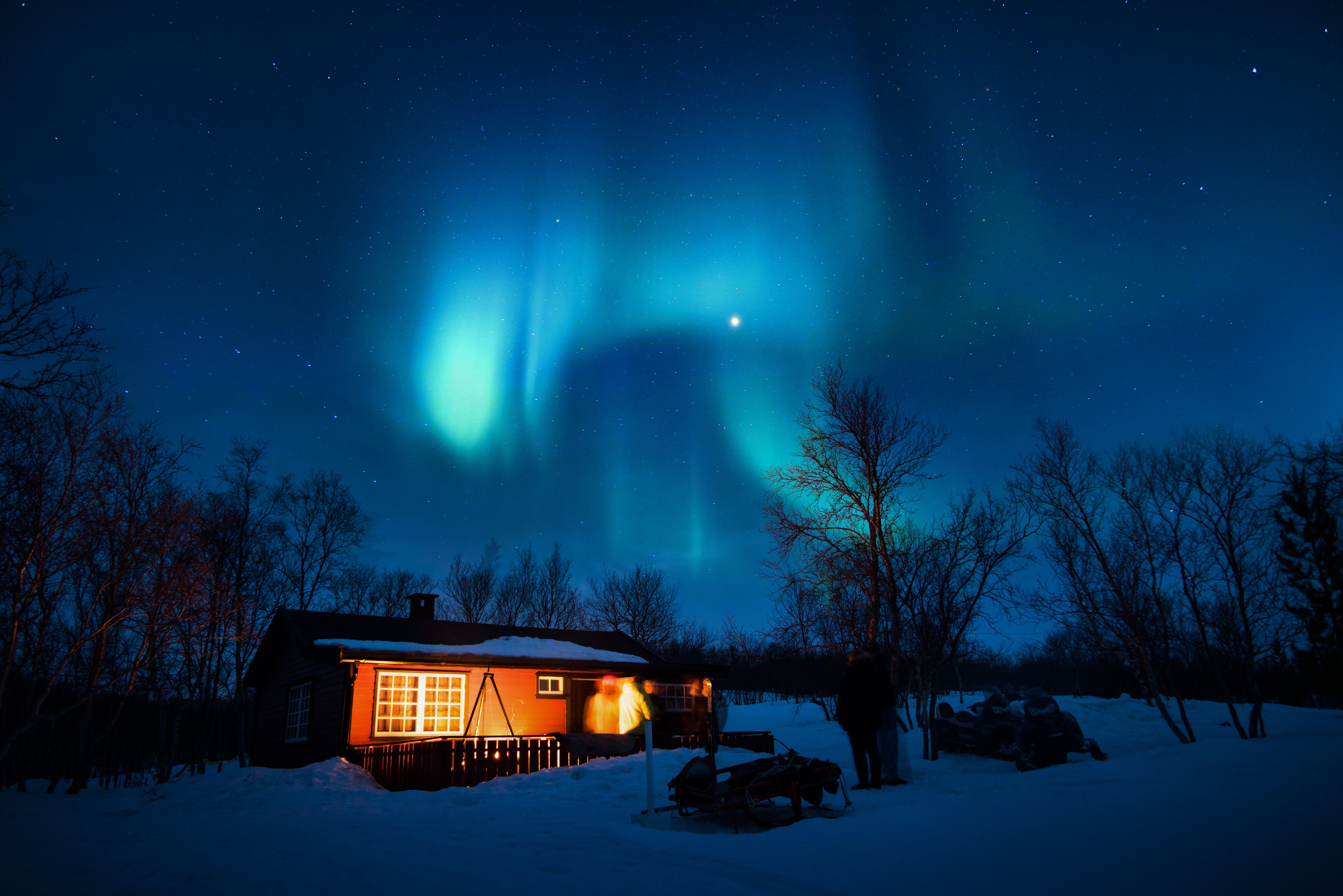 Warmly lit cabin beneath vivid northern lights on a starry Arctic winter night.