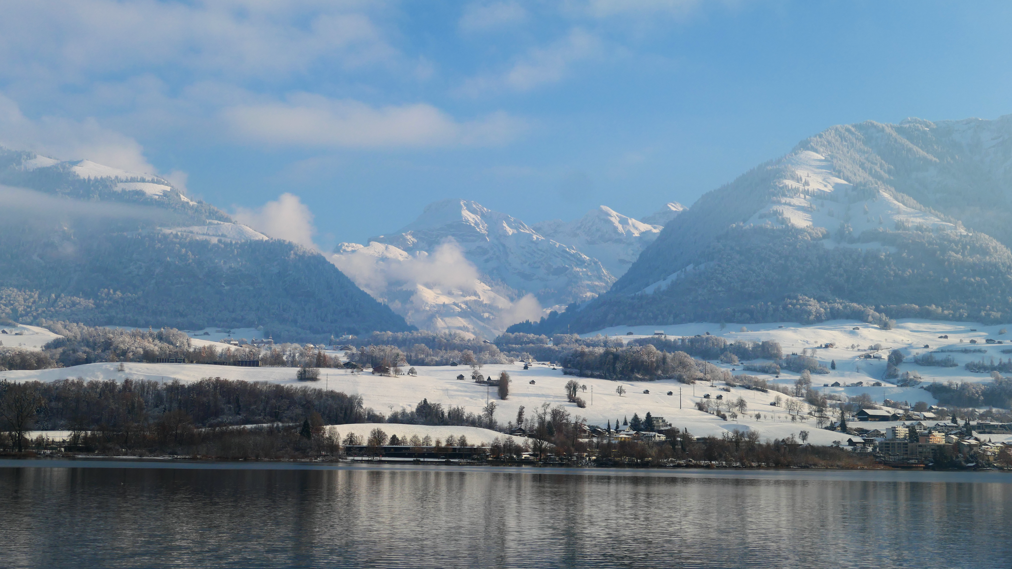 Snow-covered Swiss Alps rising above a tranquil lake near Sachseln in winter.